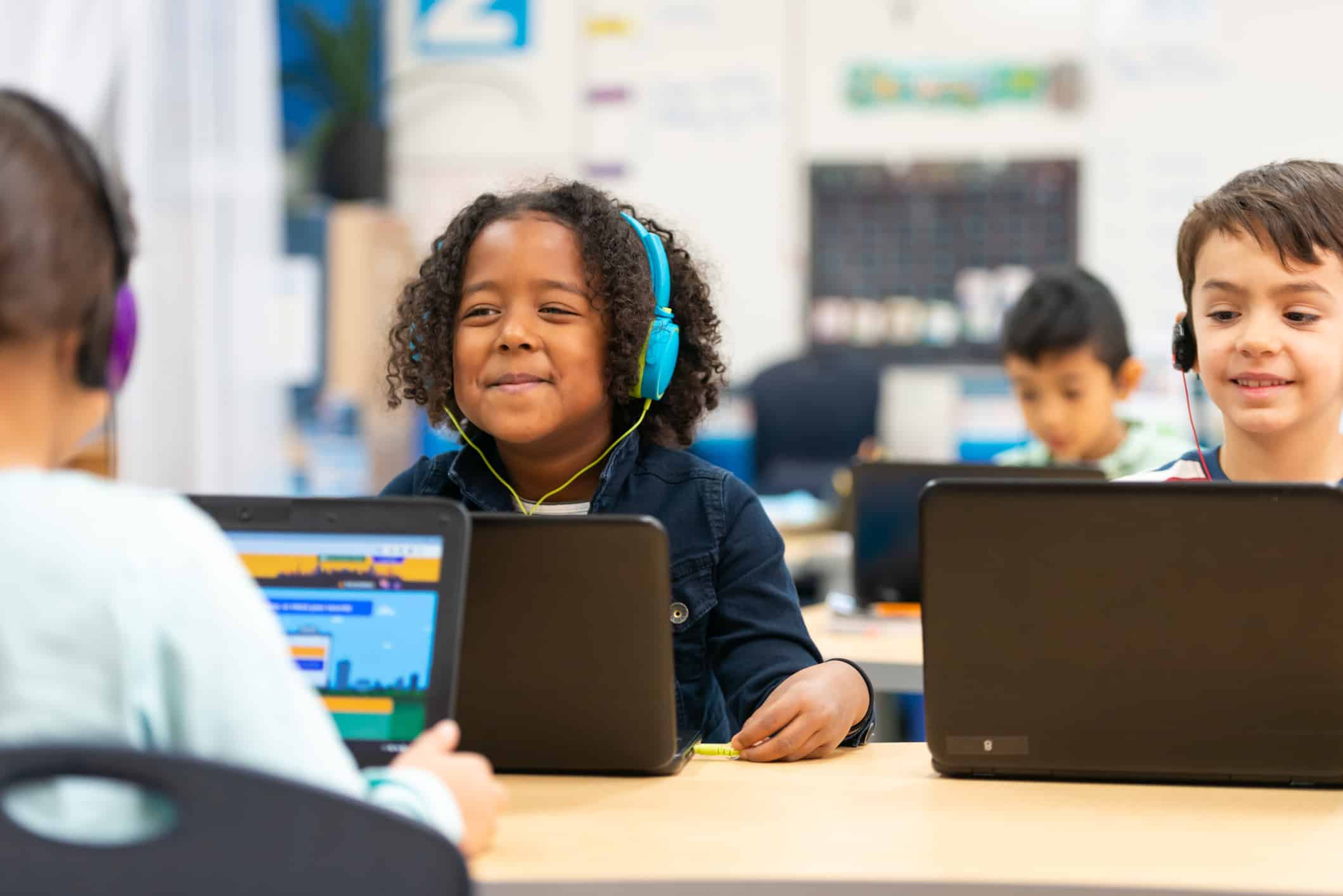 A cute little girl of African descent sits at a computer while learning about some interesting facts. The other students around her do the same, all while wearing headphones.