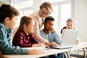 Leraar helpt leerlingen met digitale geletterdheid op een laptop in de klas, gericht op het ontwikkelen van mediawijsheid.